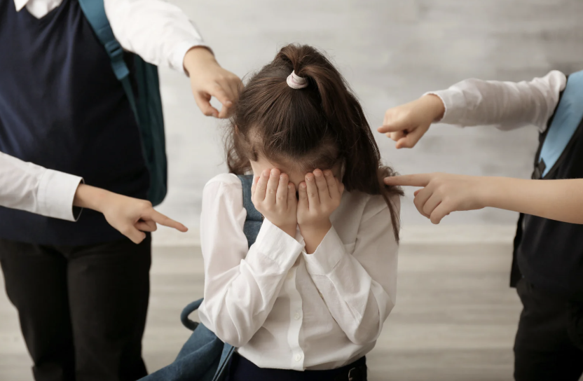 children pointing fingers at a school girl with her head in her hands